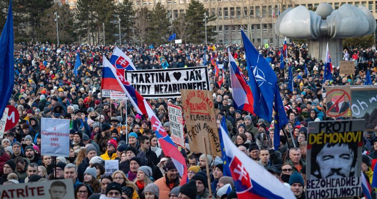 Účastníci s transparentmi a vlajkami počas spomienkového zhromaždenia k 7. výročiu vraždy Jána Kuciaka a Martiny Kušnírovej, ktoré spoločne organizujú Mier Ukrajine a Za slušné Slovensko na Námestí slobody v Bratislave. Bratislava, 21. február 2025. Foto: SITA/Jana Birošová