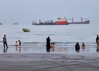 Pobrežie Hormuzského prielivu pri iránskom meste Bandar Abbas priťahuje kúpajúcich sa. V pozadí lode, čakajúce na prechod úžinou. Foto: SITA/Amirhosein Khorgooi/ISNA via AP