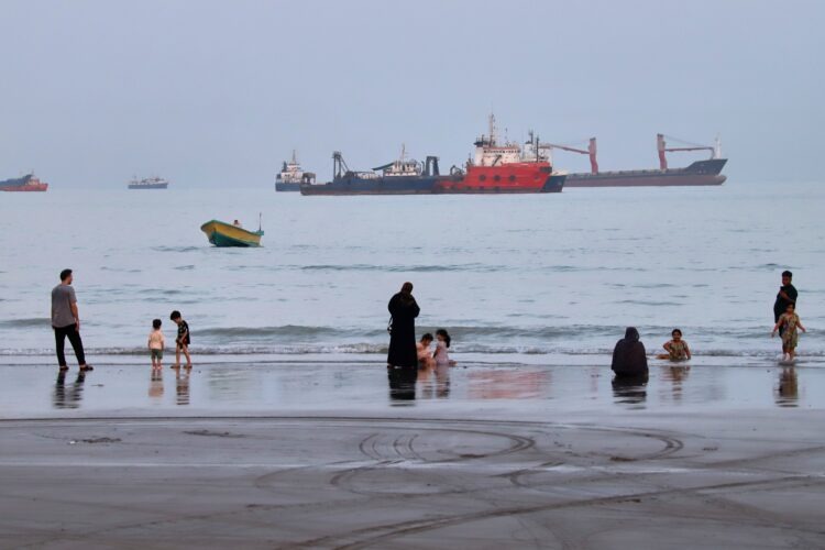 Pobrežie Hormuzského prielivu pri iránskom meste Bandar Abbas priťahuje kúpajúcich sa. V pozadí lode, čakajúce na prechod úžinou. Foto: SITA/Amirhosein Khorgooi/ISNA via AP