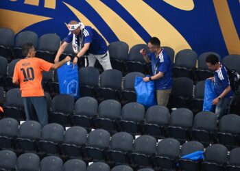 Japonskí fanúšikovia zbierajú odpadky na tribúne po júnovom zápase s Holandskom na majstrovstvách sveta vo futbale v USA. Upratovanie štadiónov je ich dlhoročným zvykom. Tento rok však rozruch vyvolali vrecia s nápisom *Japan pride*, ktoré fanúšikom poskytla hotelová sieť APA. FOTO: SITA/AP Photo/Jessica Tobias